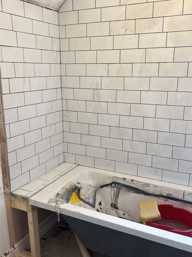Tiling under way in a bathroom, floor and wall tiles set out around the bath