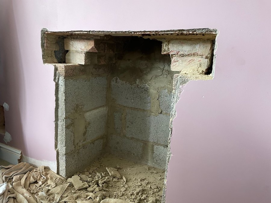 A fireplace opening cut back to bare blockwork with the old lintel removed and rubble on the floor
