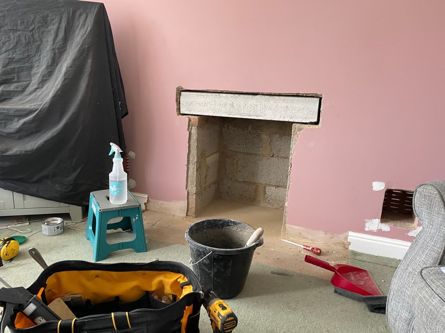 A fireplace opening squared up and swept out ready for a stove, with dust sheets and tools in the room