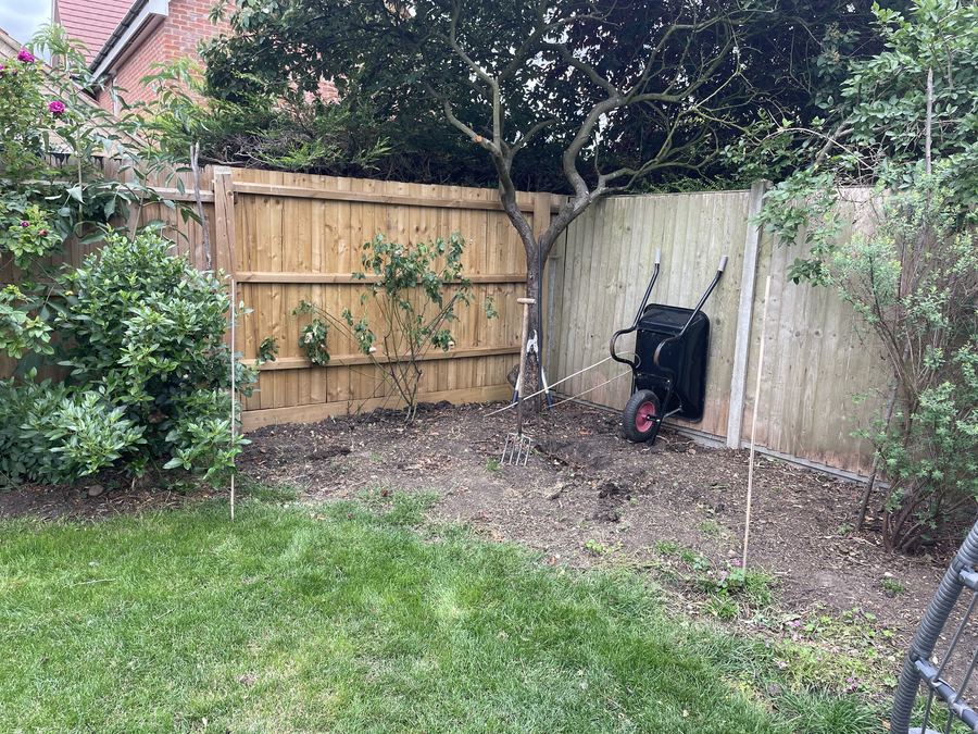 The bare corner of a garden before work, with a fence, a wheelbarrow and cleared ground