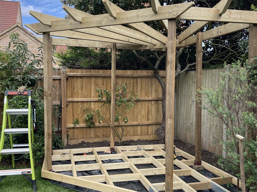 Decking boards being laid on the sub-frame under a finished pergola structure