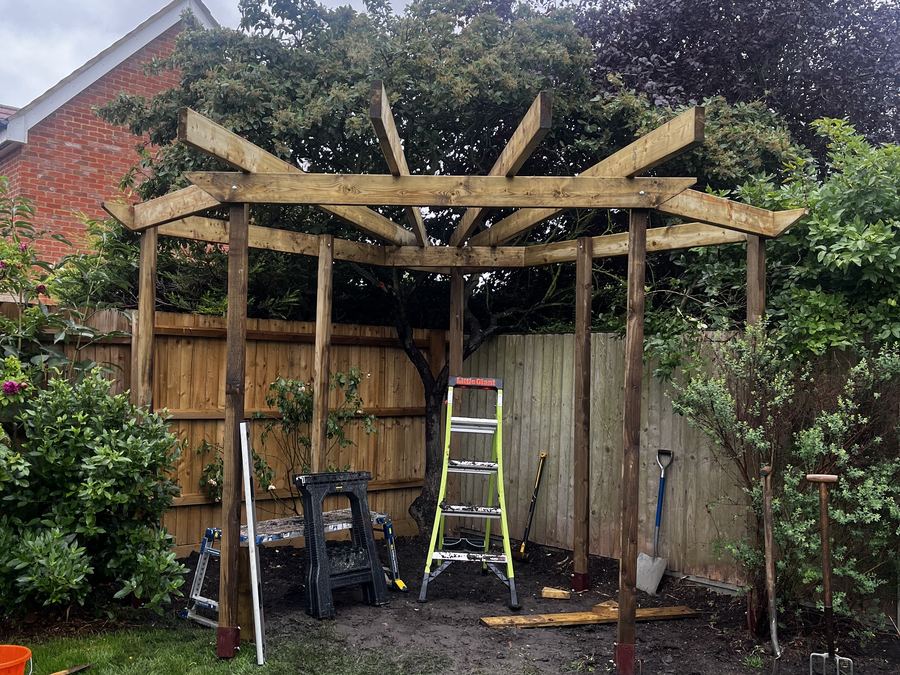 The timber frame of a garden pergola standing in place with a stepladder and tools alongside