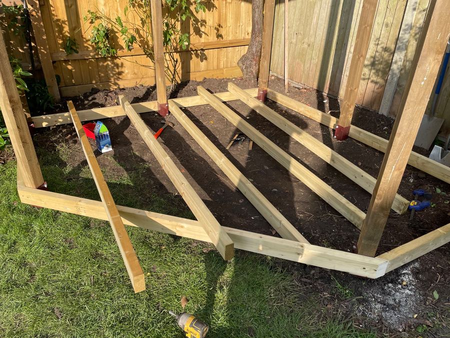 Timber deck joists set out on the ground beneath a pergola frame, ready to be levelled and fixed