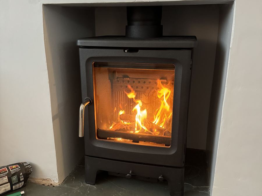 A woodburning stove installed in a finished plastered fireplace opening with a small fire lit