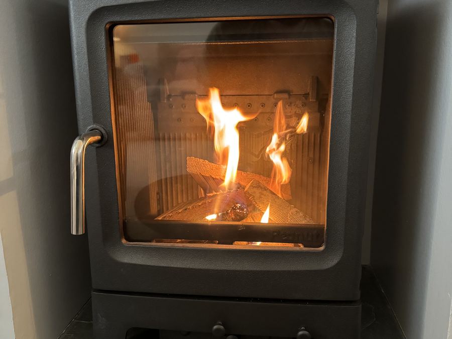A woodburning stove burning brightly on a slate hearth with logs stacked beside it