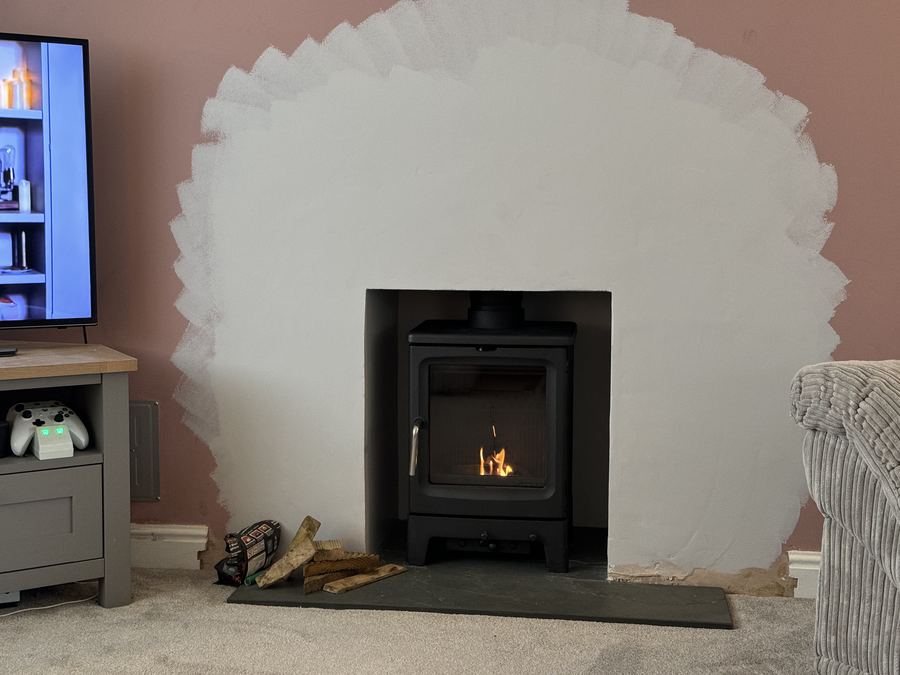 A newly formed fireplace opening with fresh plaster around a woodburning stove set into the chimney breast